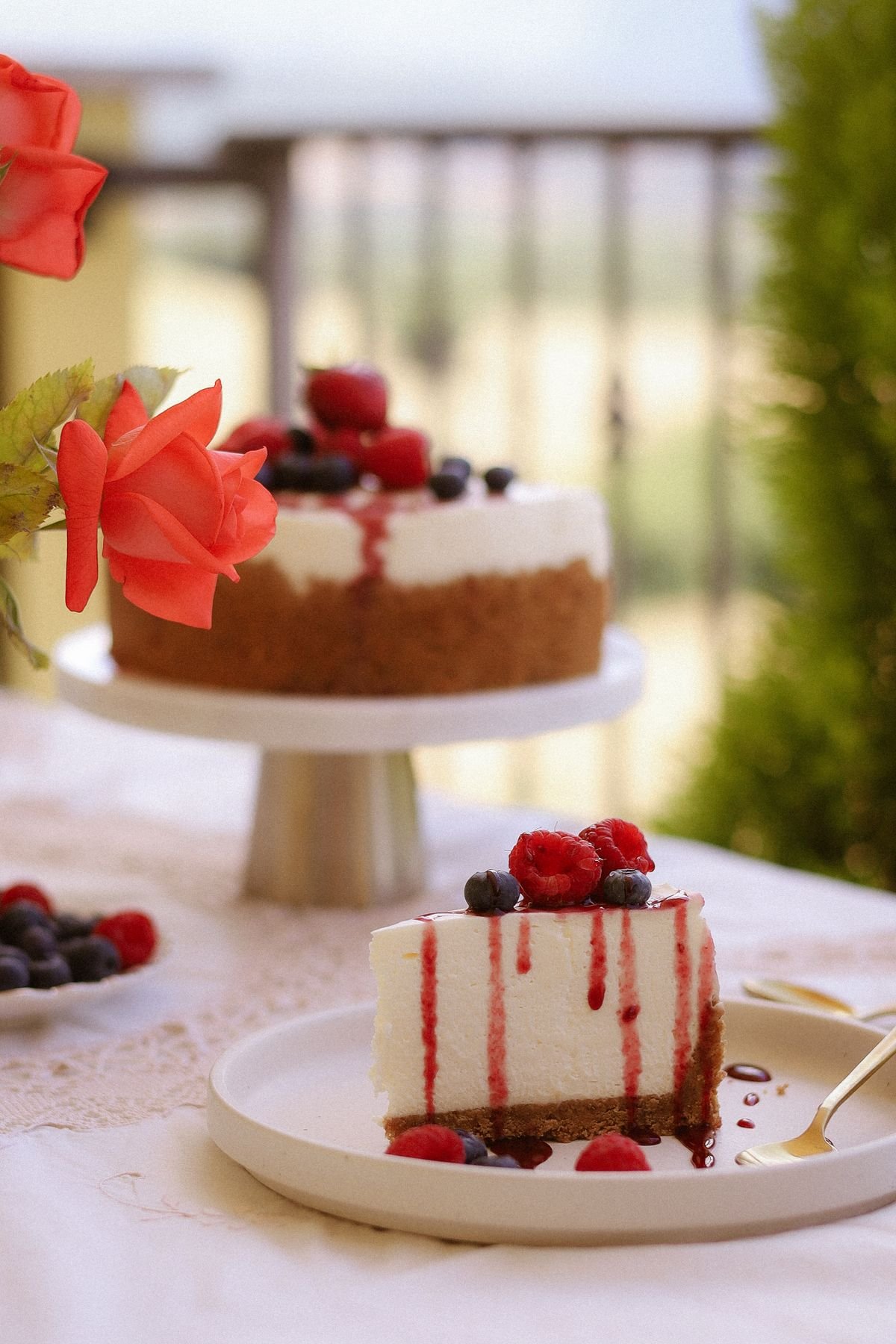 A whole cheesecake on a stand beside a slice topped with berries