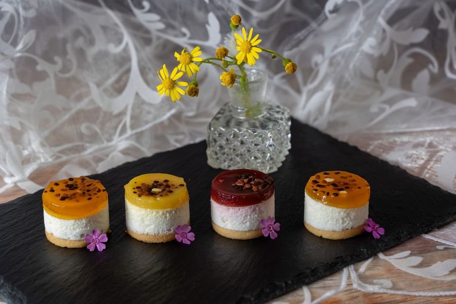 Four individual mini cheesecakes with fruit tops on a slate board